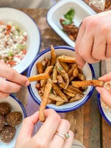 Mains qui se servent dans des plats accompagnés de frites