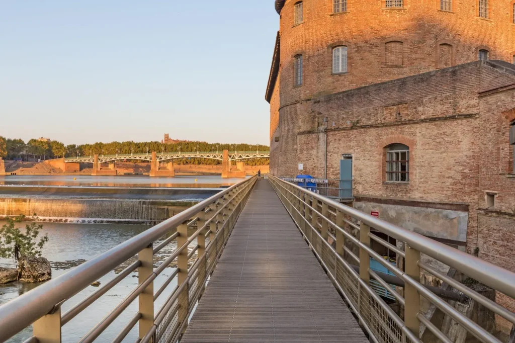 Passerelle du Bazacle à Toulouse avec vue sur la Garonne et les bâtiments historiques en briques.