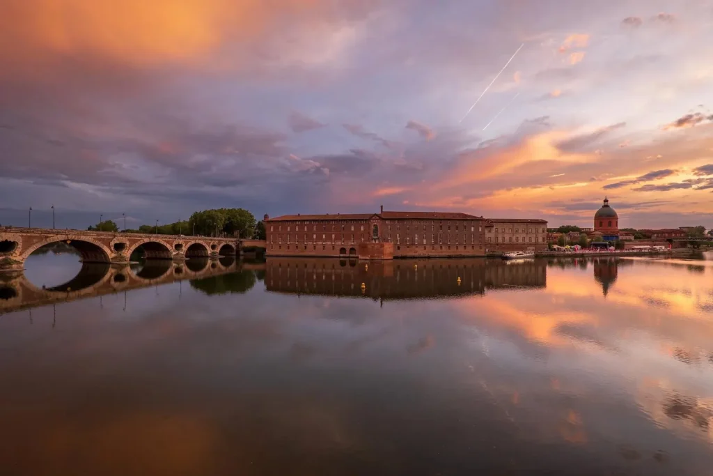 Panorama du Pont-Neuf et de la Garonne à Toulouse sous un ciel coloré au coucher du soleil.
